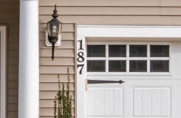 A close crop of the garage corner, with the house number 187 in black digits beside the door